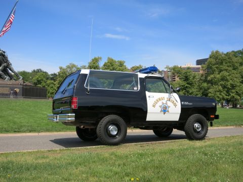 1991 Ford LTD Crown Victoria - Rear three-quarter view of a black-and-white Highway Patrol SUV parked on a path with trees and a memorial in the background.