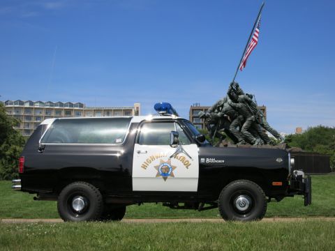 1991 Ford LTD Crown Victoria - Driver-side profile of a black-and-white Dodge Ram Charger Highway Patrol SUV parked on grass with a bronze memorial behind.