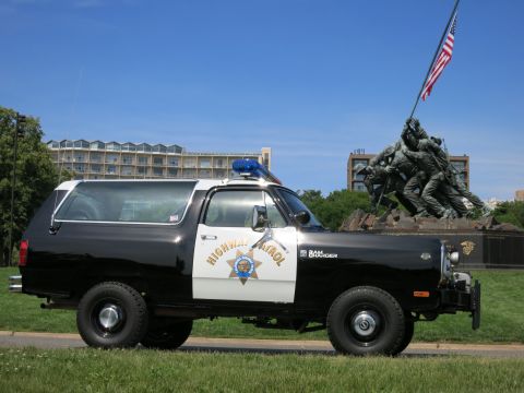 1991 Ford LTD Crown Victoria - black-and-white Dodge Ram Charger Highway Patrol SUV parked on grass in front of a flag-raising war memorial.