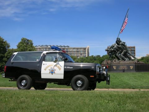 1991 Ford LTD Crown Victoria - Side view of a black-and-white Highway Patrol SUV with a front push bar parked on grass near a bronze war memorial.