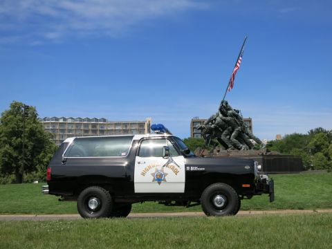 1991 Ford LTD Crown Victoria - Driver-side view of a black-and-white Highway Patrol SUV parked on grass with a war memorial and U.S. flag behind.