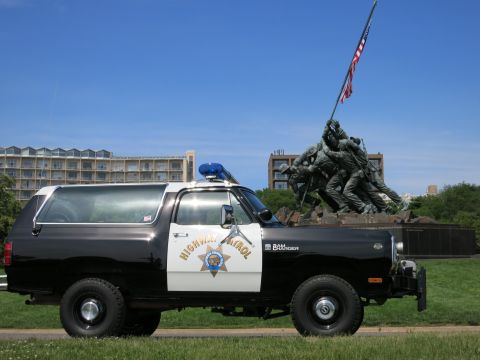 1991 Ford LTD Crown Victoria - Side view of a black-and-white Dodge Ram Charger Highway Patrol SUV parked on grass in front of a bronze war memorial.