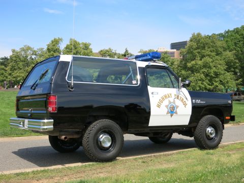 1991 Ford LTD Crown Victoria - Rear three-quarter view of a black-and-white Highway Patrol SUV parked on a paved path among green trees.