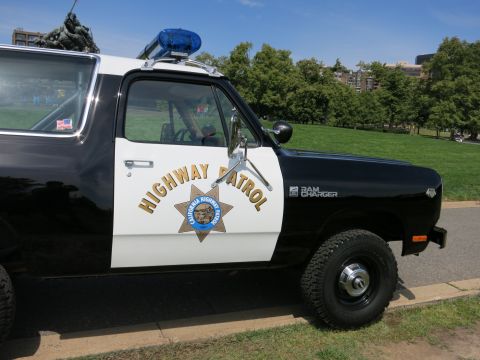 1991 Ford LTD Crown Victoria - Close-up of the gold Highway Patrol star decal and Ram Charger badge on the white door of a black-and-white patrol SUV.