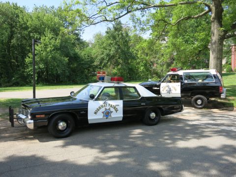 1991 Ford LTD Crown Victoria - Front-quarter view of a black-and-white Highway Patrol sedan with push bar parked under trees beside a patrol SUV.