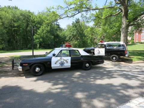 1991 Ford LTD Crown Victoria - black-and-white Highway Patrol sedan with rooftop lights parked on a shaded road alongside a matching patrol SUV.