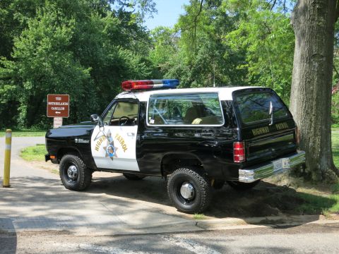 1991 Ford LTD Crown Victoria - Rear three-quarter view of a black-and-white Highway Patrol SUV parked on a shaded road beside a wooden sign.
