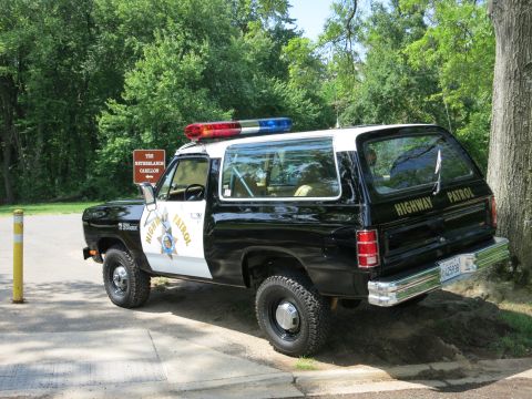 1991 Ford LTD Crown Victoria - black-and-white Dodge Ramcharger lettered Highway Patrol with a roof light bar sits parked on grass near trees.