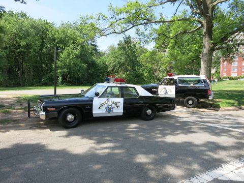 1991 Ford LTD Crown Victoria - black-and-white Highway Patrol sedan with roof lights is parked in a park, a marked SUV visible behind it.