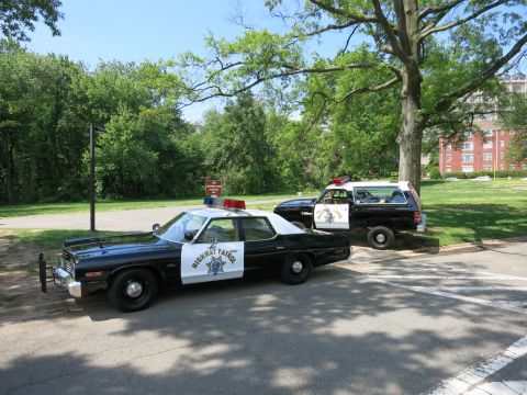 1991 Ford LTD Crown Victoria - black-and-white Highway Patrol four-door sedan with a roof light bar sits in a park with a marked SUV behind it.