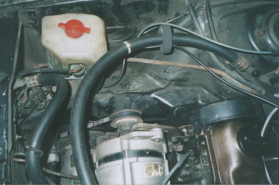 Engine bay with alternator, black hoses, and coolant tank with red cap