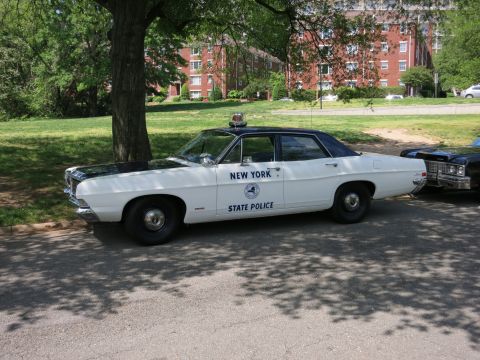1991 Ford LTD Crown Victoria - white-and-black Ford sedan lettered New York State Police with a single roof light sits parked under a tree.