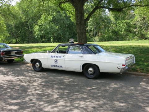 1991 Ford LTD Crown Victoria - white Ford sedan lettered New York State Police with a roof beacon sits in a park with another car at the left.