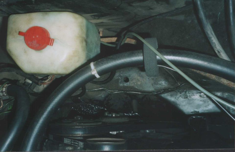 Engine bay with white coolant tank, red cap, black hoses and drive belt