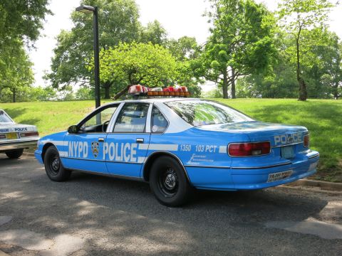 1991 Ford LTD Crown Victoria - blue NYPD police sedan marked 'NYPD POLICE 1350 103 PCT' shows its rear three-quarter angle with a roof light bar.