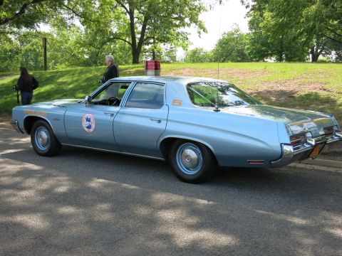 1991 Ford LTD Crown Victoria - light-blue 1970s full-size sedan in police livery with a single red roof beacon, door agency seal and unit number 5 parked on a road.
