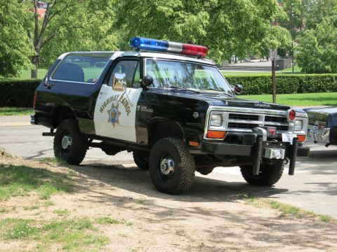 1991 Ford LTD Crown Victoria - black-and-white Dodge Ramcharger marked 'HIGHWAY PATROL' with a star door emblem, roof light bar and front winch parked on grass.