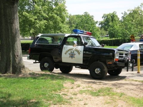 1991 Ford LTD Crown Victoria - black-and-white Dodge Ramcharger marked 'HIGHWAY PATROL' with a star door emblem sits beside a large tree on a park road.