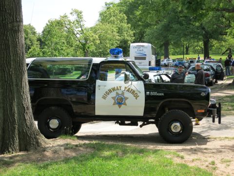 1991 Ford LTD Crown Victoria - lifted black-and-white Dodge Ramcharger lettered 'HIGHWAY PATROL RAM CHARGER' with a star emblem parked among trees and other cars.