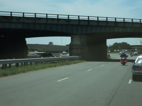 1991 Ford LTD Crown Victoria - weathered concrete highway overpass spans the road as a police motorcycle and dark sedan travel beneath it.