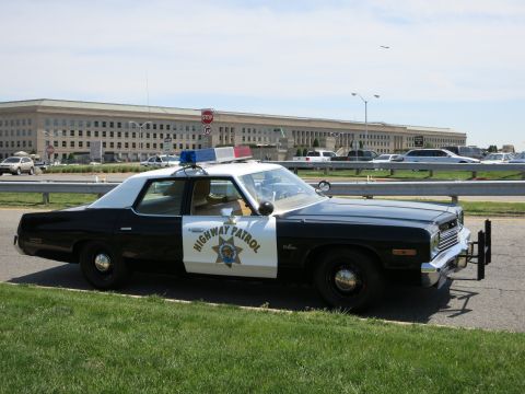1991 Ford LTD Crown Victoria - black-and-white Dodge 'HIGHWAY PATROL' sedan with a star emblem and push bumper parked on grass before the Pentagon building.
