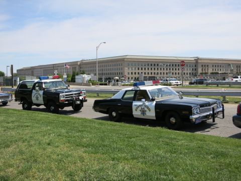 1991 Ford LTD Crown Victoria - black-and-white Dodge Highway Patrol sedan and a matching Ramcharger SUV parked on a lawn in front of the Pentagon building.