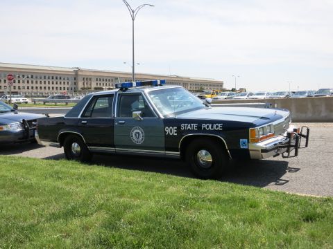 1991 Ford LTD Crown Victoria - dark-blue and gray State Police sedan marked 90E with a push bumper and roof lightbar sits before the Pentagon.