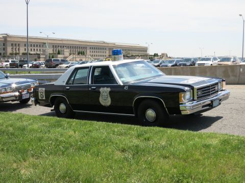 1991 Ford LTD Crown Victoria - black-and-white police sedan numbered 45 with a gold badge door decal and roof lights is parked outside the Pentagon.