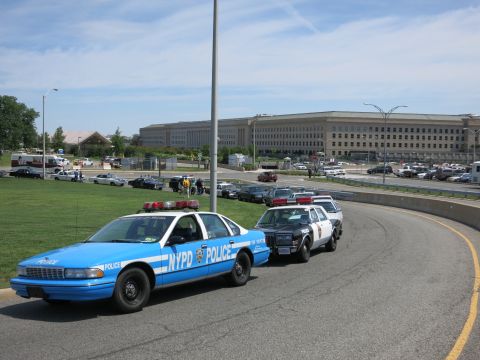 1991 Ford LTD Crown Victoria - blue NYPD Police sedan leads a line of marked cruisers along a curving road in front of the Pentagon.