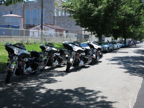 1991 Ford LTD Crown Victoria - line of police touring motorcycles is parked at the curb of a tree-shaded street with patrol cars behind them.