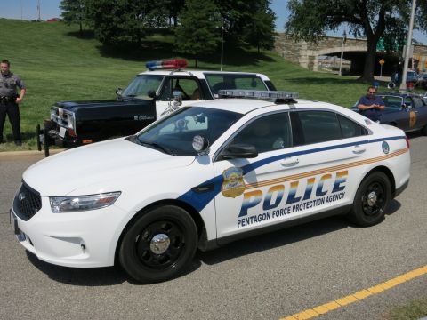 1991 Ford LTD Crown Victoria - white Ford Police sedan lettered Pentagon Force Protection Agency with blue striping is parked beside a grassy hill.