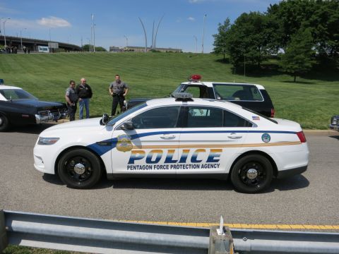 1991 Ford LTD Crown Victoria - Side view of a white Ford Police sedan marked Pentagon Force Protection Agency parked on a road with officers nearby.