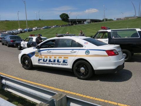 1991 Ford LTD Crown Victoria - Rear-quarter view of a white Ford Police sedan lettered Pentagon Force Protection Agency among other cruisers on a road.
