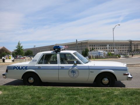 1991 Ford LTD Crown Victoria - boxy white-and-blue police sedan marked POLICE with unit number 839 parked on grass near the Pentagon.
