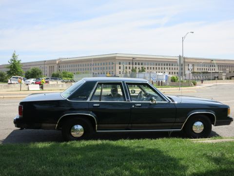 1991 Ford LTD Crown Victoria - black full-size Ford four-door sedan parked in profile on a curb with the Pentagon behind it.