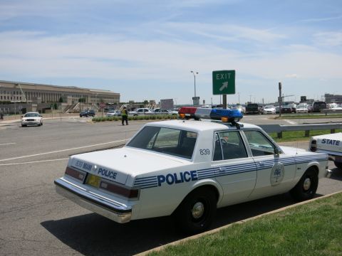 1991 Ford LTD Crown Victoria - Rear three-quarter view of a white-and-blue POLICE sedan, unit 839, with a light bar parked near a green Exit sign.