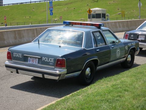 1991 Ford LTD Crown Victoria - Rear quarter view of a two-tone blue STATE POLICE Ford sedan with light bar parked beside a grassy embankment.