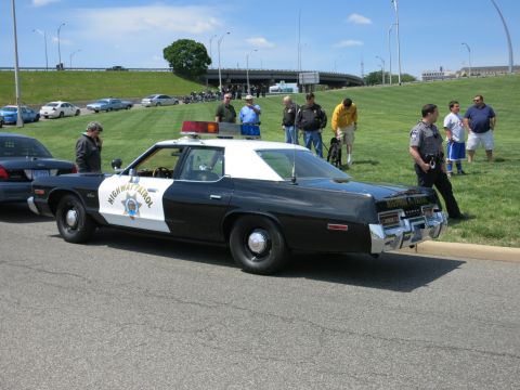 1991 Ford LTD Crown Victoria - black-and-white Dodge Highway Patrol sedan parked at a curb as several people stand and chat beside it.