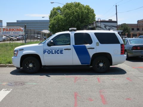 1991 Ford LTD Crown Victoria - white Federal Protective Service Police Chevrolet Tahoe SUV with a blue stripe parked on a lot.