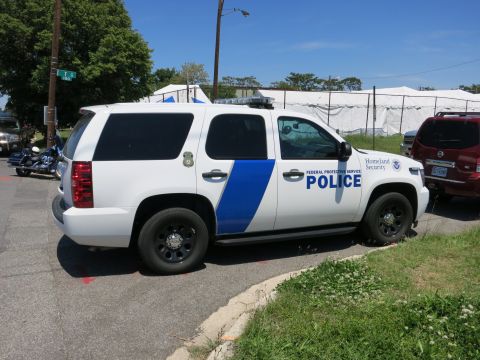 1991 Ford LTD Crown Victoria - white Federal Protective Service Police Chevrolet Tahoe SUV bearing a Homeland Security marking parked beside tents.