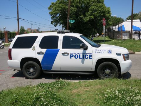 1991 Ford LTD Crown Victoria - white Federal Protective Service Police Chevrolet Tahoe SUV with Homeland Security markings parked near a stop sign.