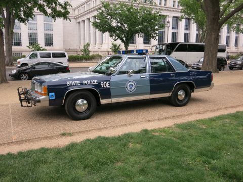 1991 Ford LTD Crown Victoria - blue-and-silver Massachusetts State Police Ford LTD Crown Victoria marked STATE POLICE 90E parked before a stone building.
