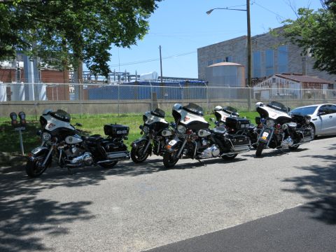 1991 Ford LTD Crown Victoria - Several police touring motorcycles parked in a row along a lot in front of industrial buildings and tanks.