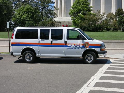 1991 Ford LTD Crown Victoria - white Nassau County Police Chevrolet Express van with orange-and-blue stripes parked near a columned memorial.