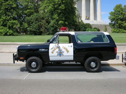 1991 Ford LTD Crown Victoria - black-and-white Highway Patrol SUV badged Ram Charger sits curbside with a red beacon on its roof.