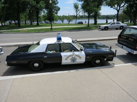 1991 Ford LTD Crown Victoria - black-and-white Highway Patrol full-size sedan sits in profile at the curb beside a tree-lined waterfront.