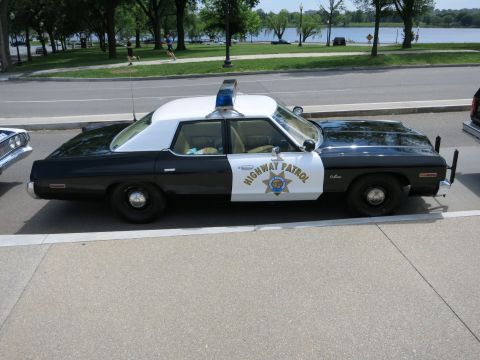 1991 Ford LTD Crown Victoria - black-and-white Highway Patrol full-size sedan with roof light bar sits in profile near a riverside park.