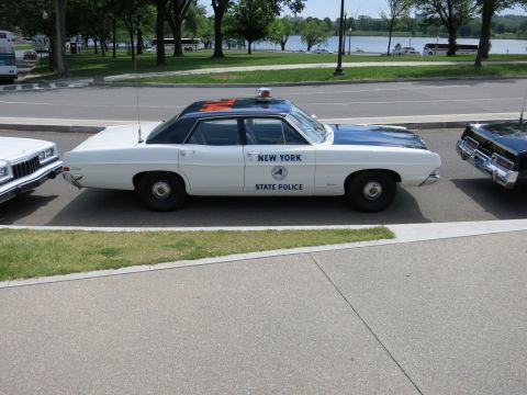 1991 Ford LTD Crown Victoria - white-and-blue 'New York State Police' sedan with roof lights sits in profile near a tree-lined waterfront.