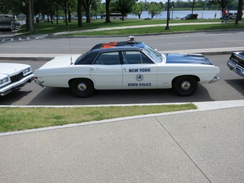 1991 Ford LTD Crown Victoria - white-and-blue 'New York State Police' full-size sedan is parked in profile beside a waterfront roadway.