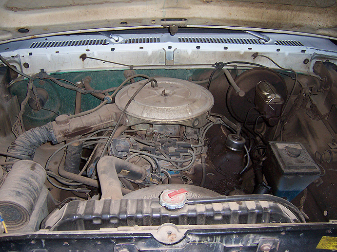Dusty engine bay with round air cleaner, V8 engine, brake booster, and radiator with red cap